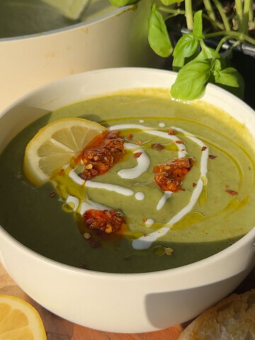 Green soup in a white bowl drizzled with some white sauce and chili oil.