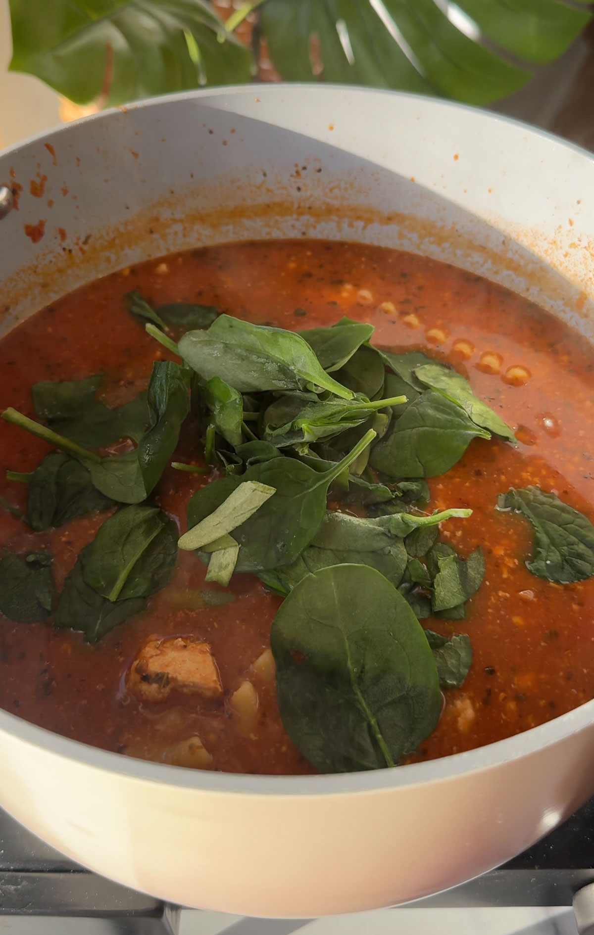 Soup in a pot with spinach on top.