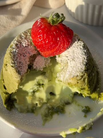 A matcha lava cake on a plate cut so the middle pools out.