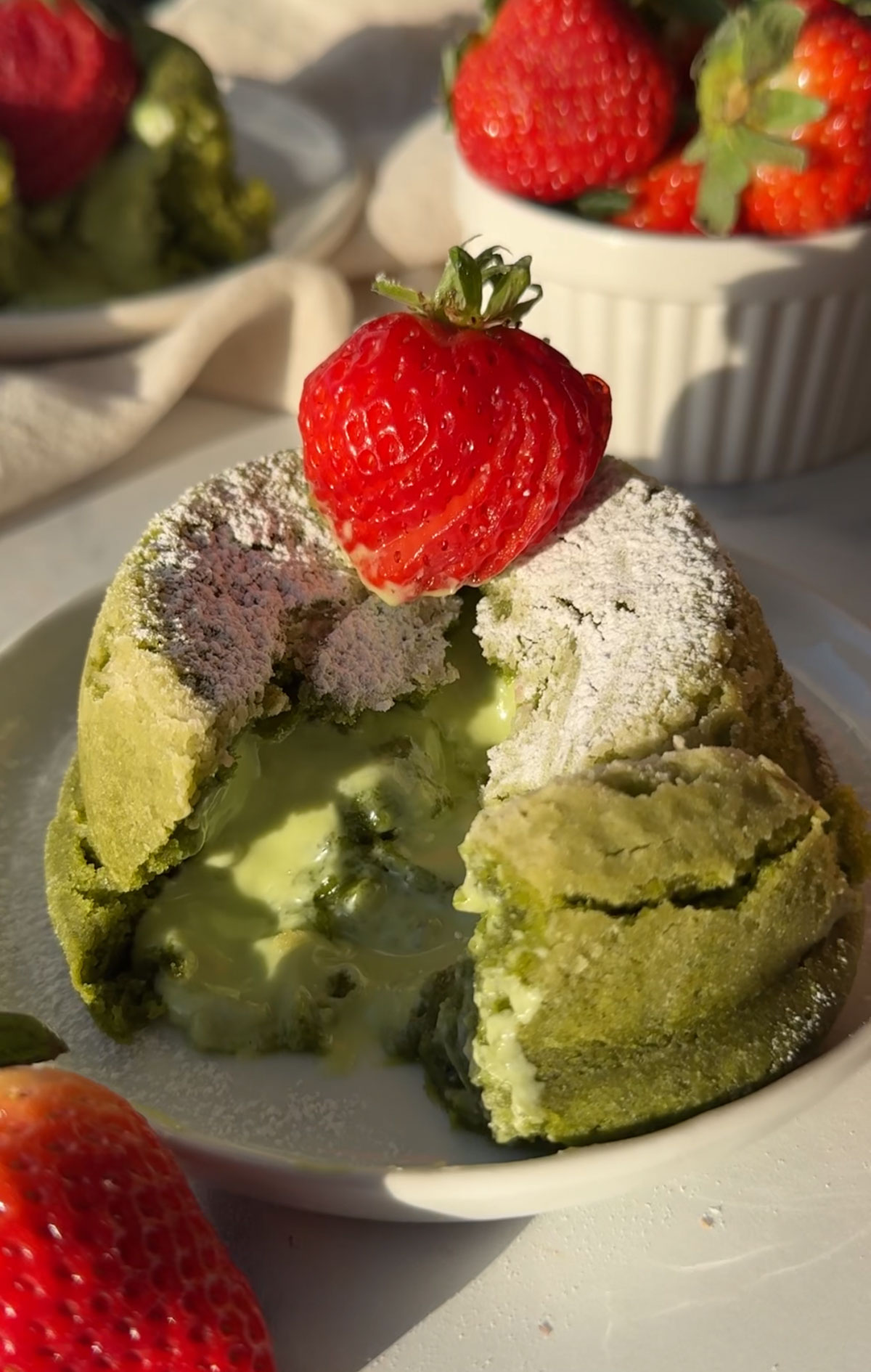 A matcha lava cake topped with a strawberry that's been cut and the molten center is melting. 