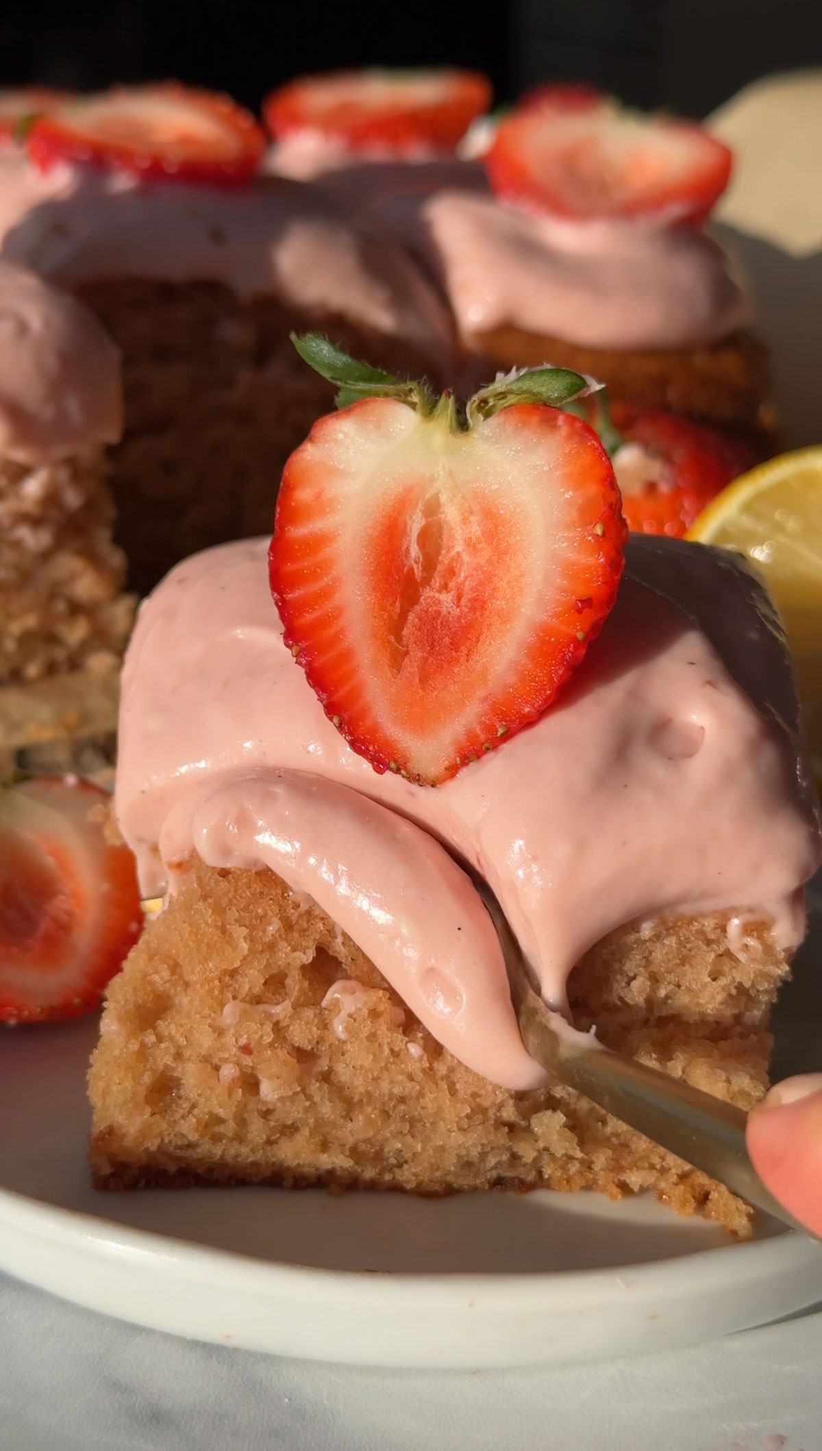 A fork cutting a bite of vegan strawberry cake on a plate.