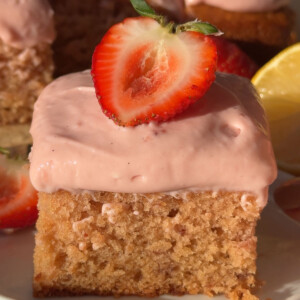 A slice of frosted vegan strawberry cake topped with half a fresh strawberry.