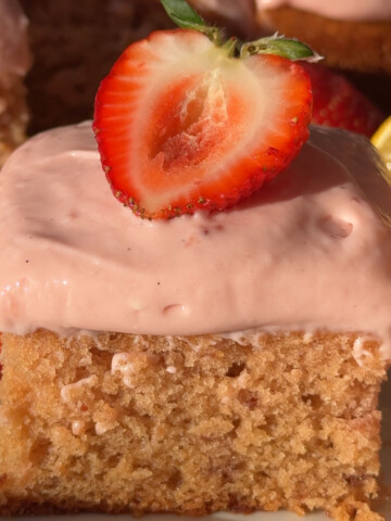 A slice of frosted vegan strawberry cake topped with half a fresh strawberry.