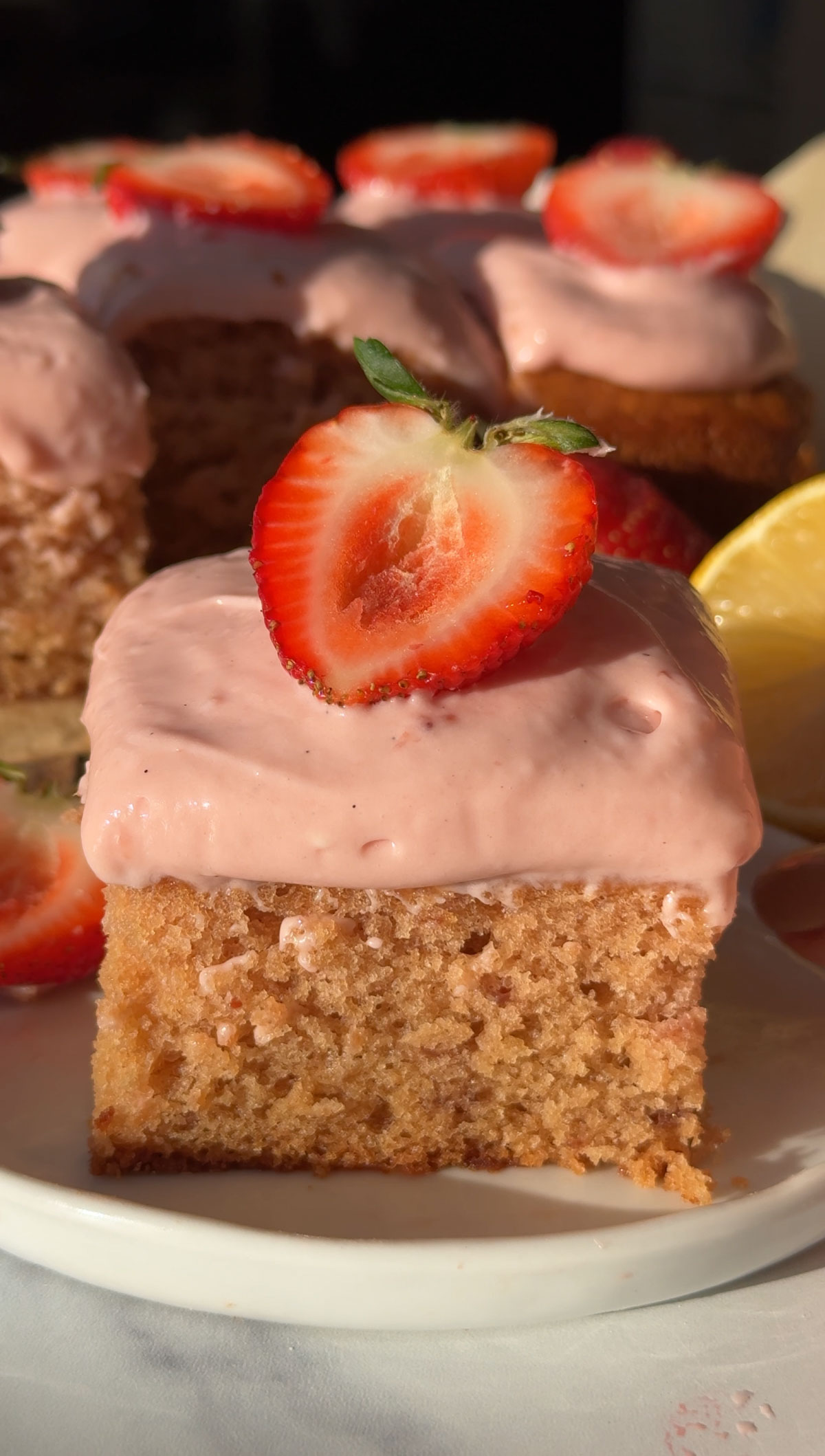 A slice of vegan strawberry cake on a plate topped with pink icing and a fresh berry.