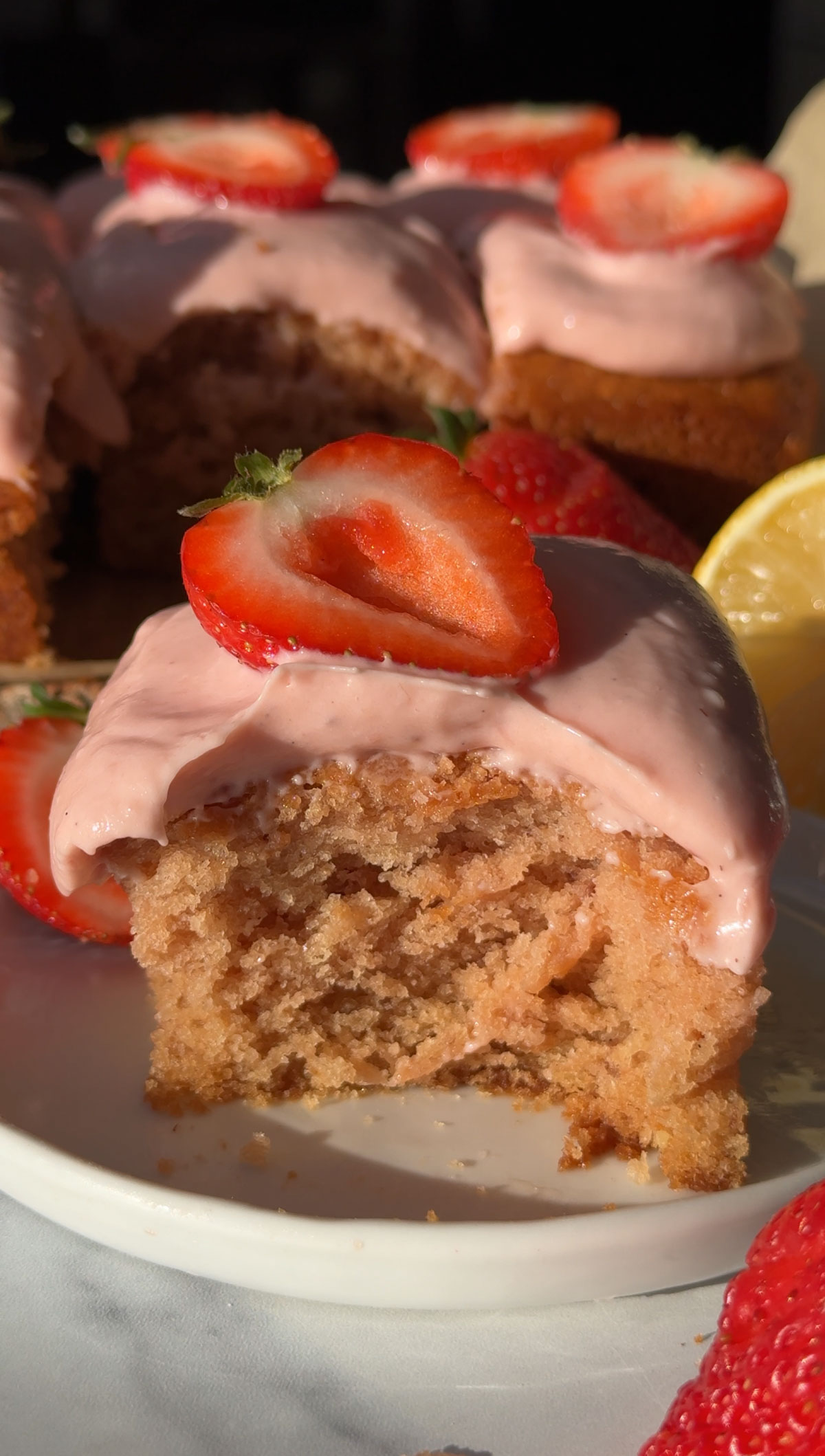 A square of vegan strawberry cake on a plate with a bite missing.