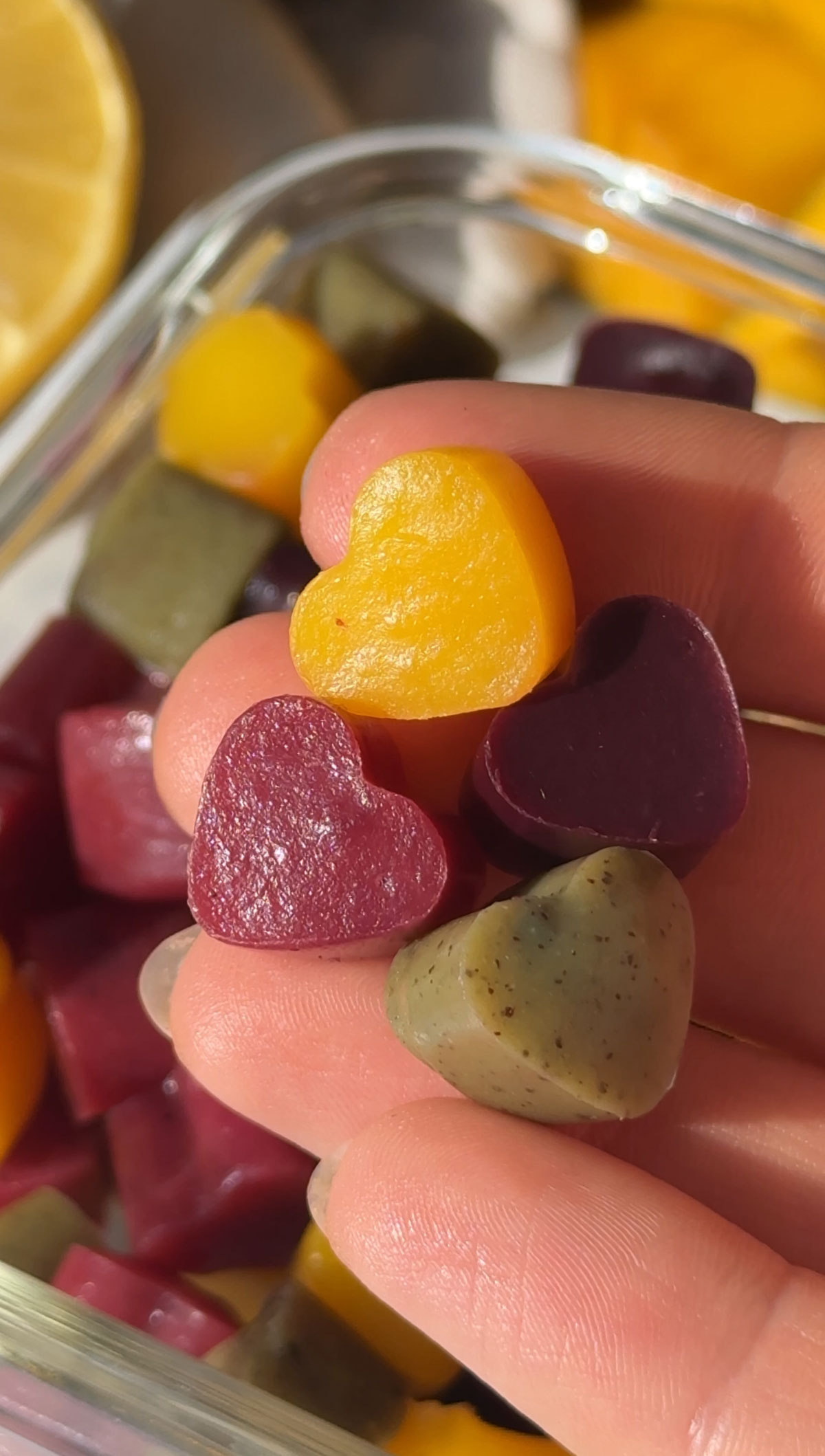 A hand holding three heart shaped vegan gummies.