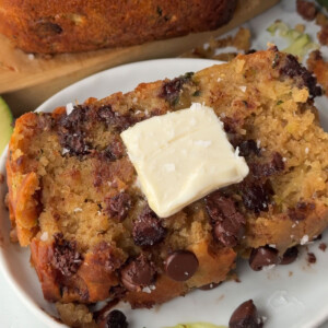 A slice of vegan zucchini bread on a plate topped with a pat of vegan butter.