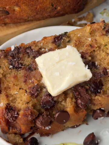 A slice of vegan zucchini bread on a plate topped with a pat of vegan butter.