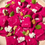 Beet pasta on a plate sprinkled with vegan feta, walnuts and basil.