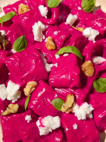 Beet pasta on a plate sprinkled with vegan feta, walnuts and basil.