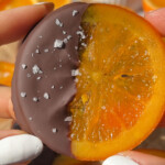 A hand holding up a candied orange slice that with one half covered in chocolate.