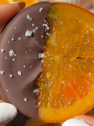 A hand holding up a candied orange slice that with one half covered in chocolate.