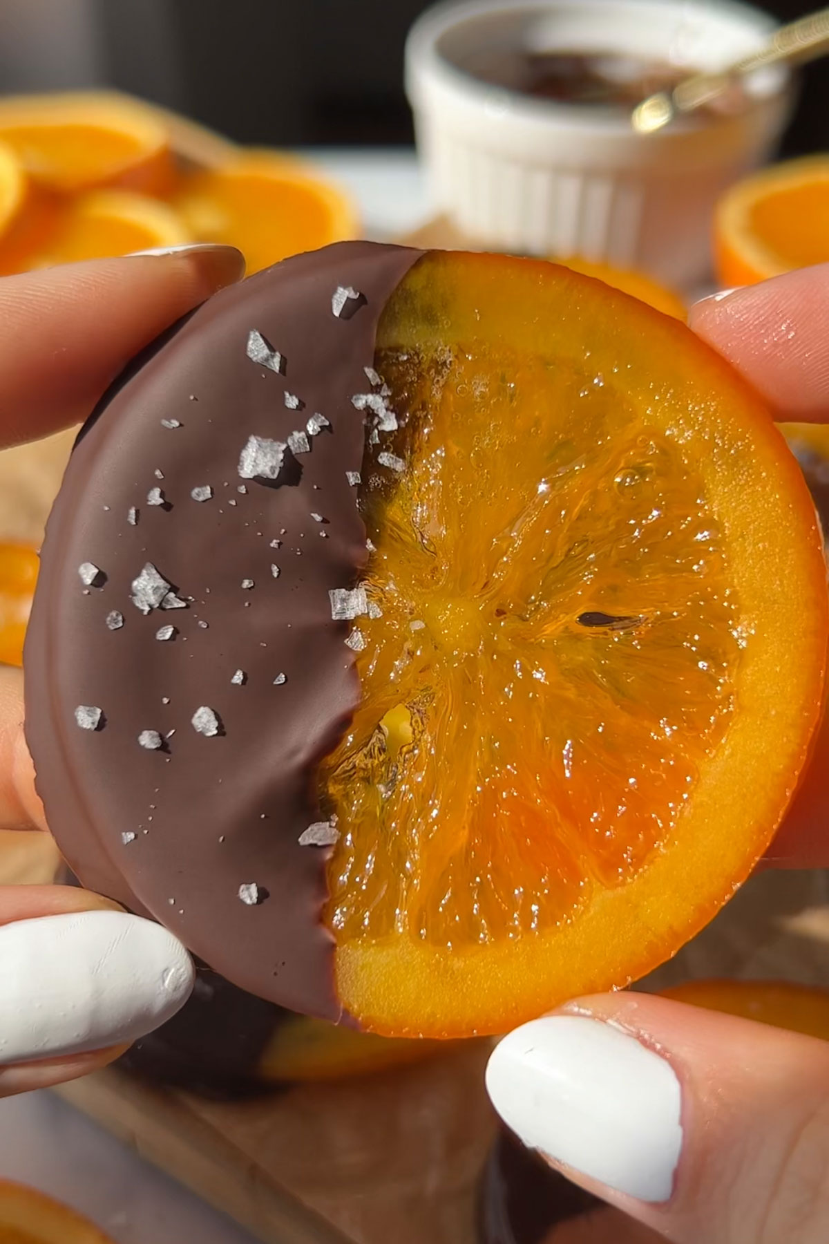 A hand holding up a candied orange slice that with one half covered in chocolate.