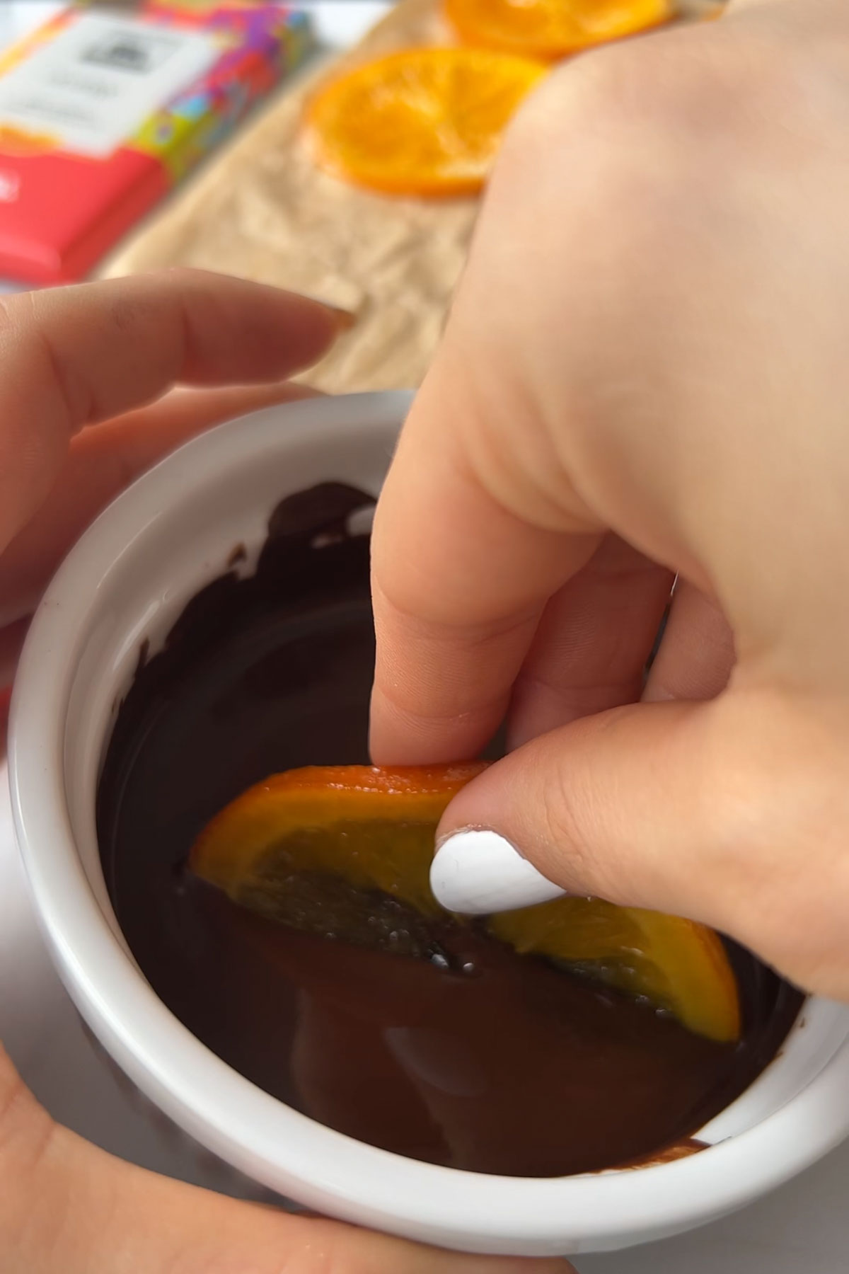 An orange slice being dipped into melted chocolate.
