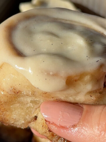 A hand holding up a glazed vegan cinnamon roll.