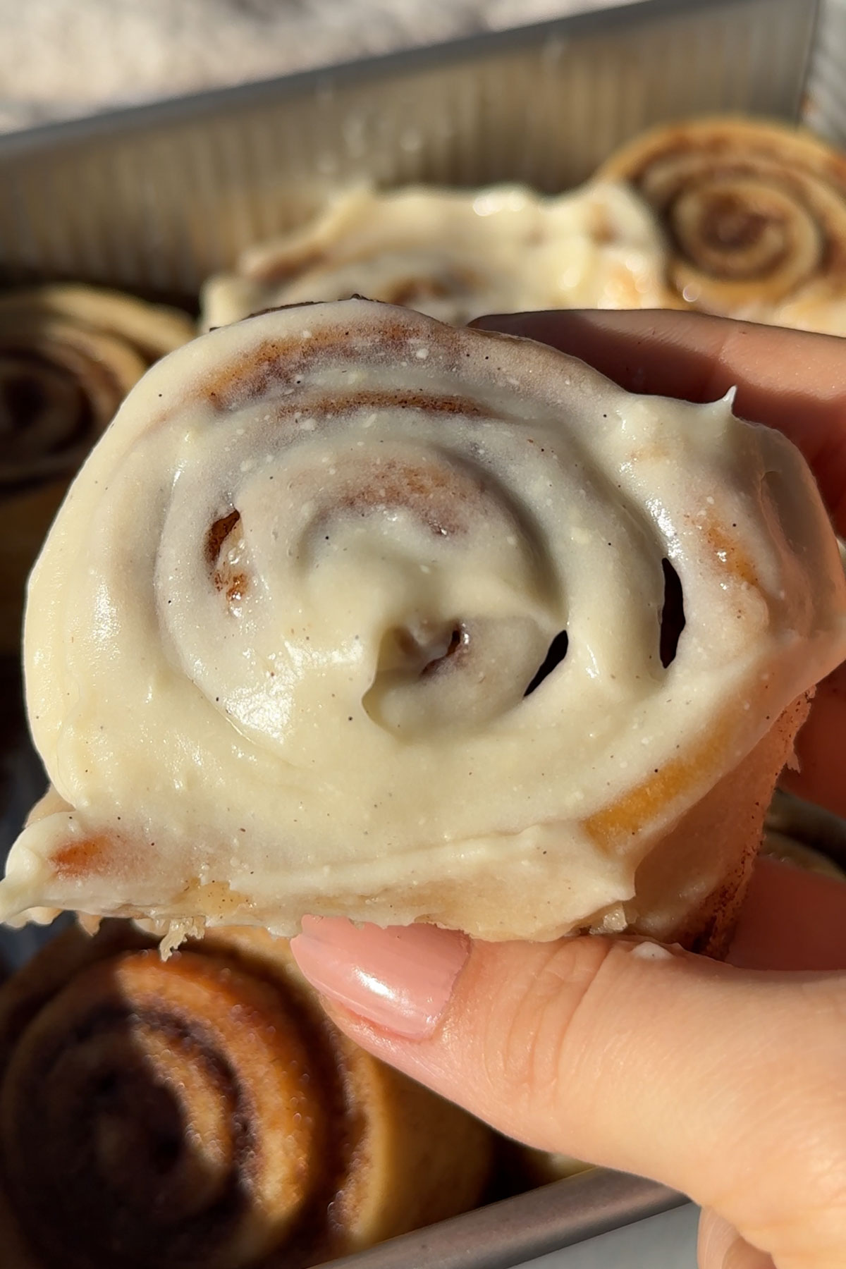 A hand holding up a glazed vegan cinnamon roll.