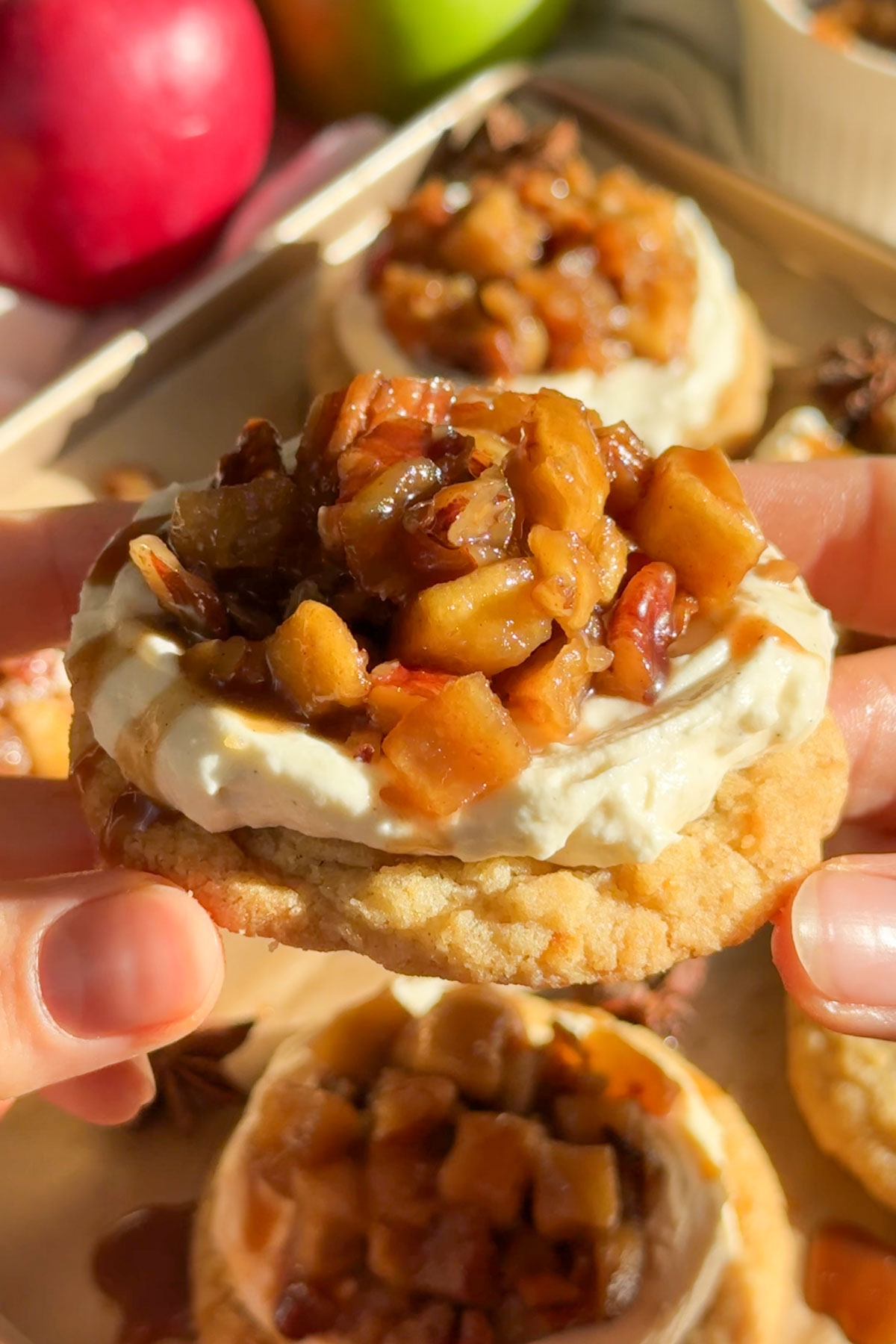 A cheesecake cookie with apples being held up in the air.