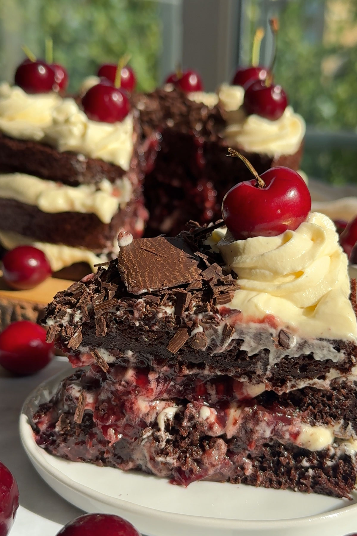 A slice of German black forest cake with icing and cherries in the middle and a cherry on top.