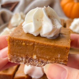 A vegan pumpkin bar topped with whipped cream held up in the air.