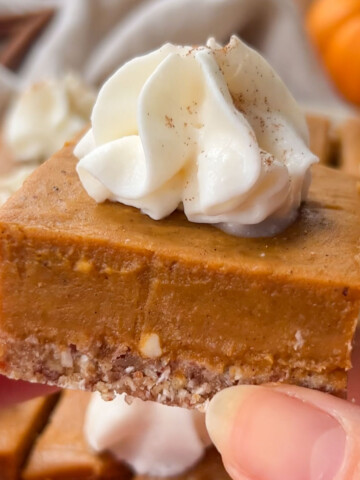 A vegan pumpkin bar topped with whipped cream held up in the air.