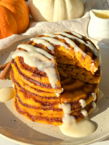 A slice taken out of a stack of pumpkin cinnamon roll pancakes.