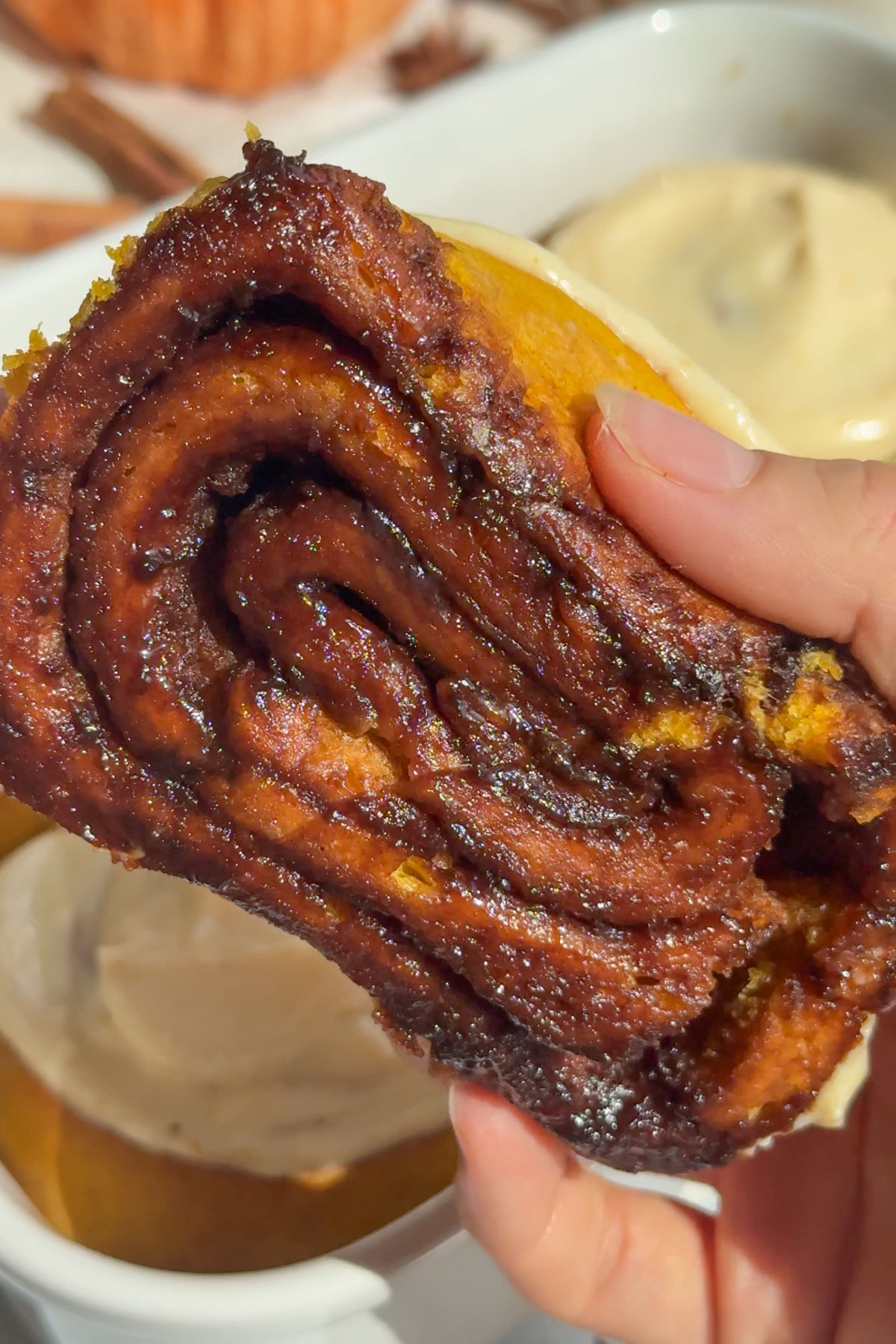 A hand holding up a pumpkin cinnamon roll without icing on it. 