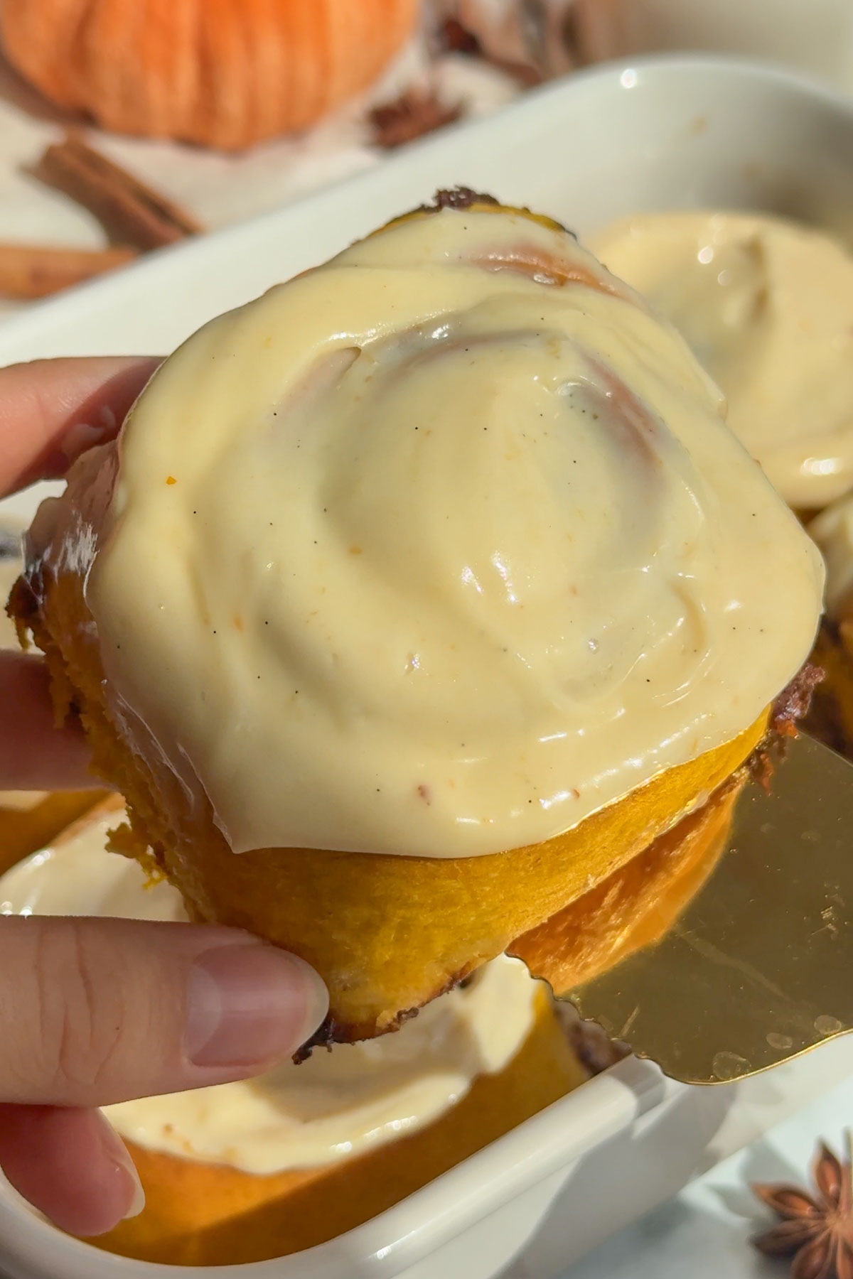 A hand holding up a pumpkin cinnamon roll with icing.