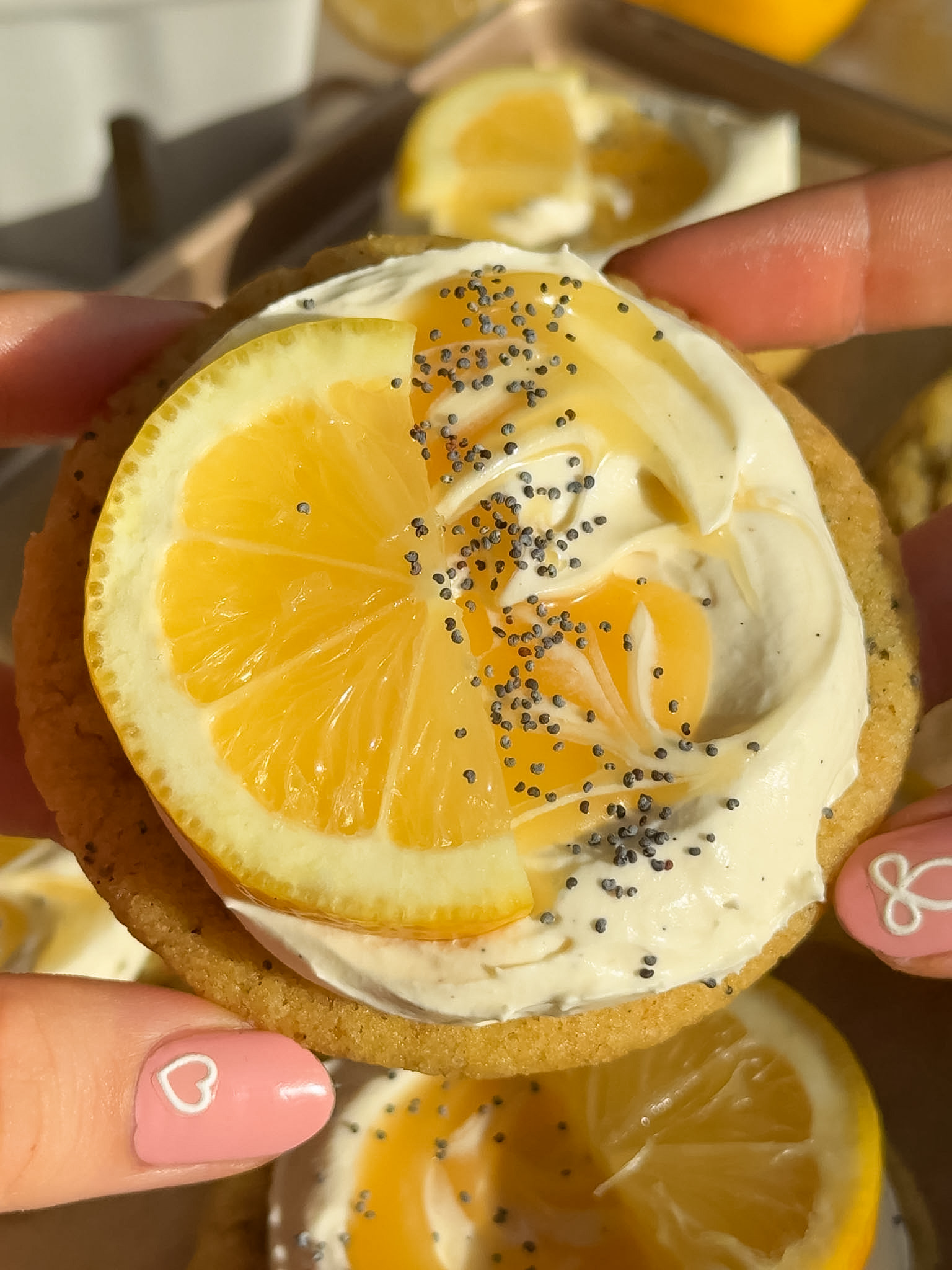 Vegan lemon cookie being held up in the air garnished with poppy seeds and a lemon slice.