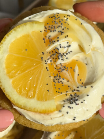 A hand holding up a vegan lemon cookie in the air.