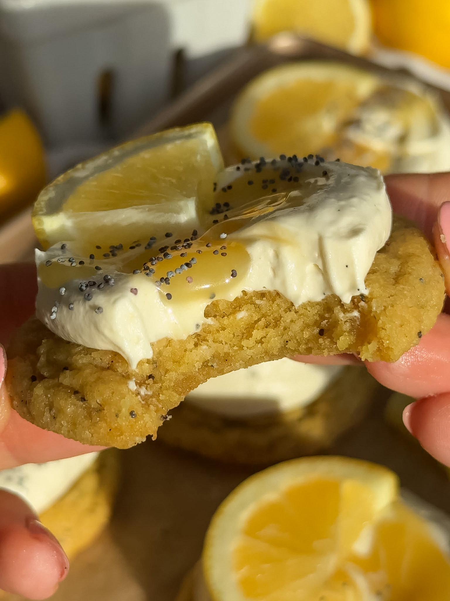 A bite taken out of a lemon cookies with cheesecake topping and a slice of lemon on top.