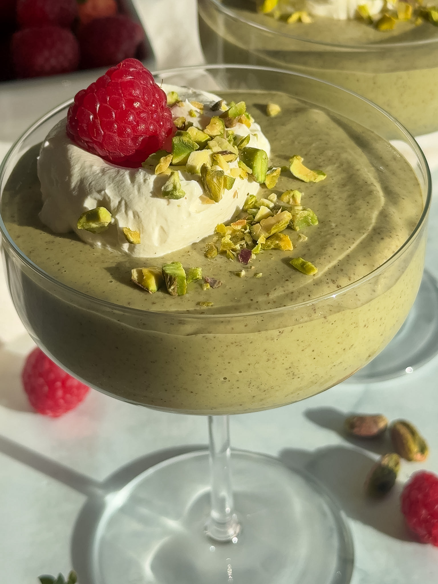 Pistachio chia pudding in a glass cup garnished with whipped cream and a fresh raspberry.