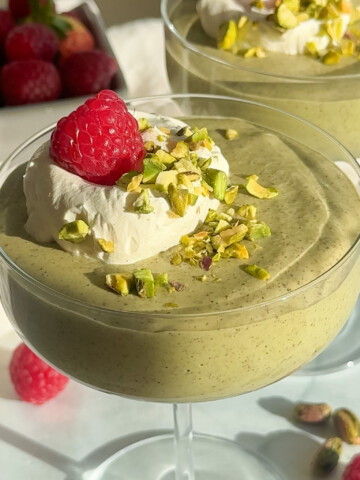 Pistachio chia pudding with whipped topping and a raspberry.